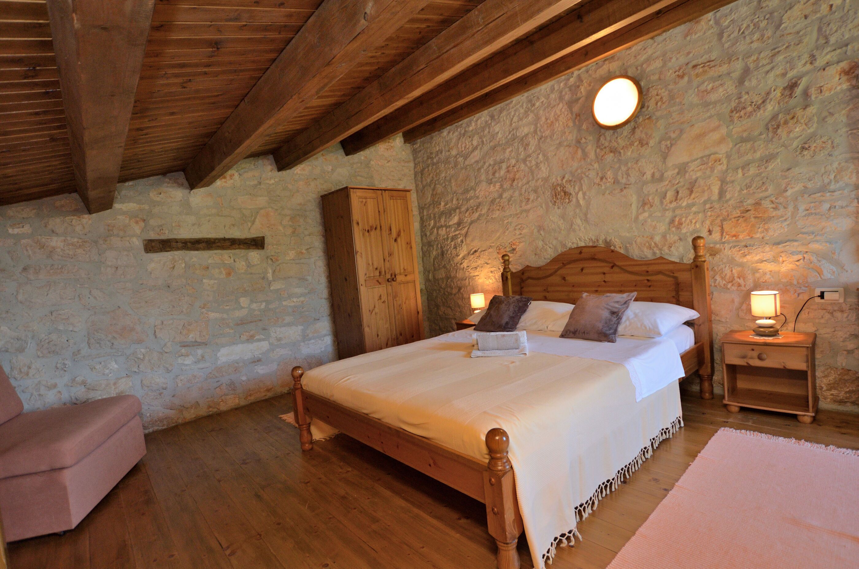 Ein Schlafzimmer mit einem hölzernen Bett, Steinwänden, einem Holzschrank und einem Nachttisch mit Lampe.