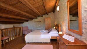 A bedroom with a wooden ceiling, stone walls, a bed with white linens, a wooden dresser, and a large mirror. - House Mariano (Lasici)