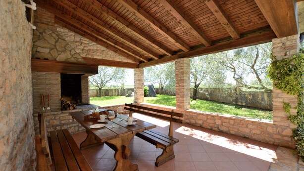An outdoor patio with a stone fireplace, wooden benches, and a table set for dining. - House Mariano (Lasici)