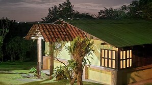 Una pequeña casa con techo de tejas y estructura de madera al frente, rodeada de hierba y árboles.