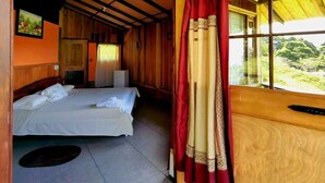 Una habitación de madera con una cama, una mesita y un ventanal con cortinas.