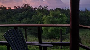 Una terraza de madera con banco y barandilla que da a un paisaje verde y exuberante durante el atardecer.