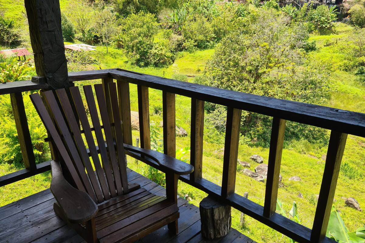 A wooden deck with a bench and a railing overlooking a lush green landscape.