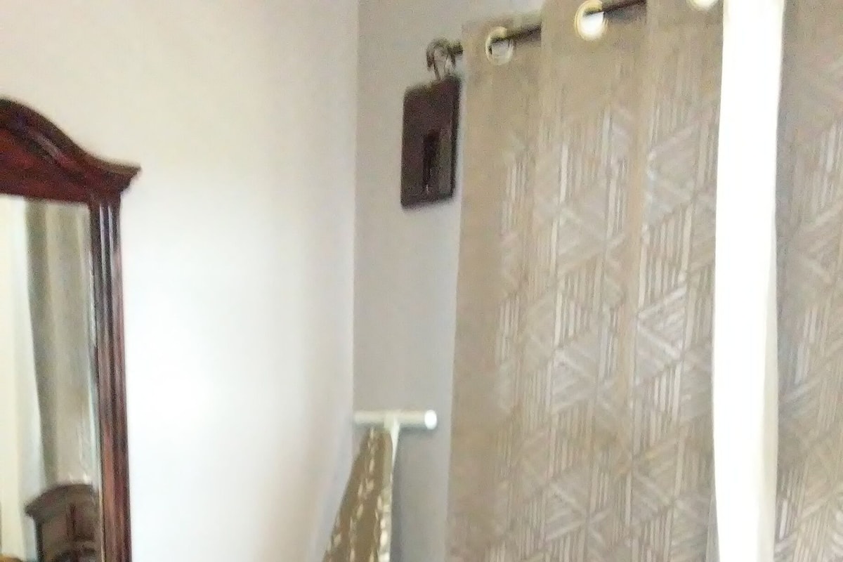 A bedroom with a large bed, a wooden dresser, a mirror, and a patterned curtain.