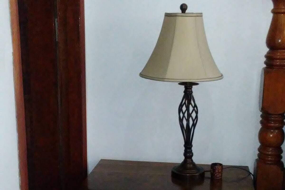 A wooden bedside table with a lamp, drawers, and a small object on top.
