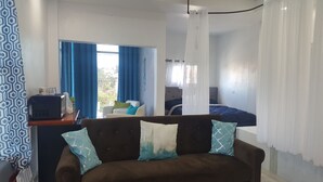 A bedroom with a bed, a sofa, a desk with a computer, and a window with curtains. - DB Towers (Belize City)