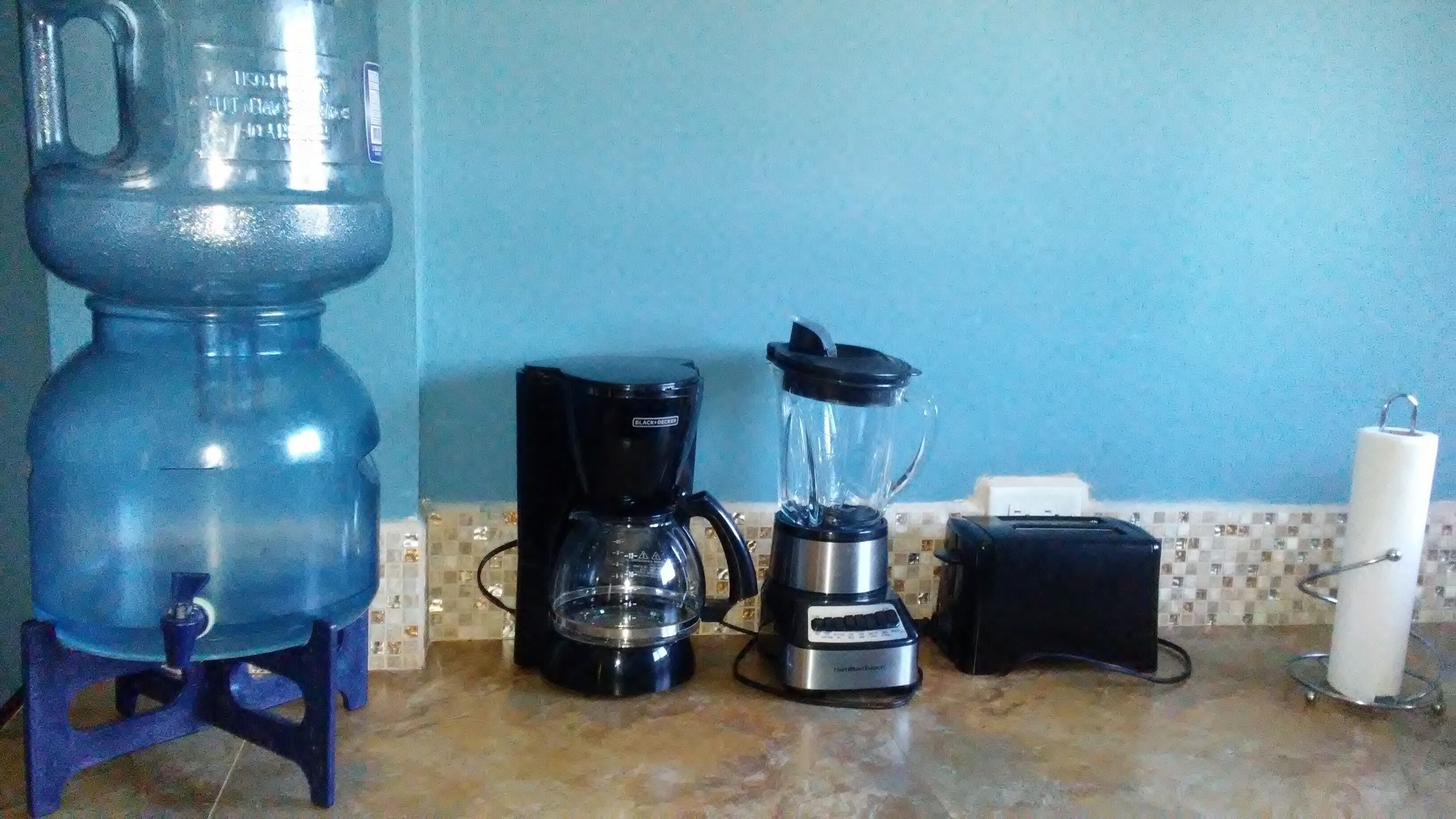 Una cocina con un dispensador de agua grande, una cafetera y una licuadora sobre la encimera.