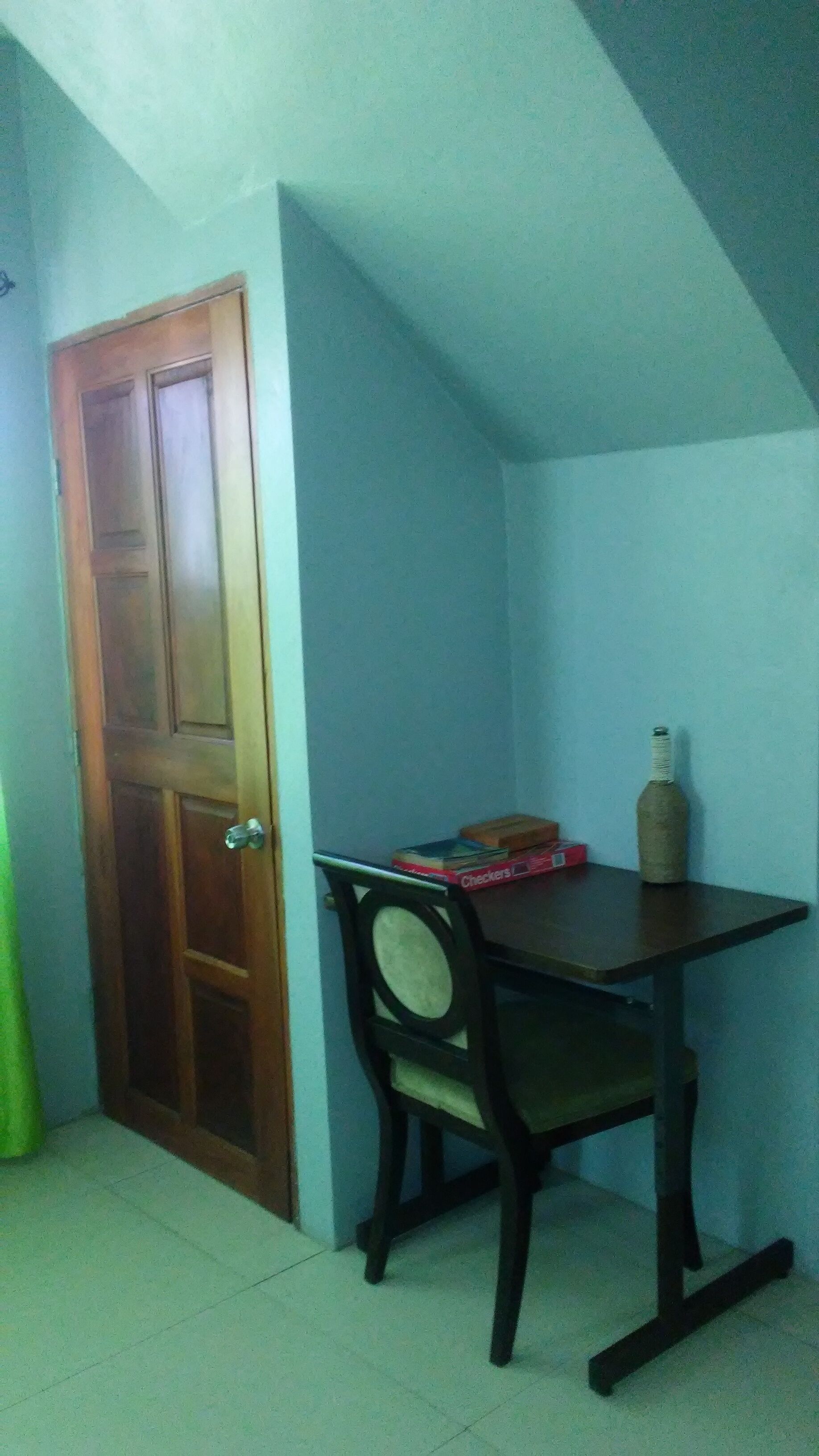 Ein Zimmer mit Holztür, einem kleinen Tisch mit Stuhl und einer Flasche auf dem Tisch.