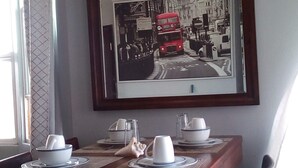 A dining area with a wooden table set for four, a framed black and white photo on the wall, and a window with curtains. - DB Towers (Belize City)