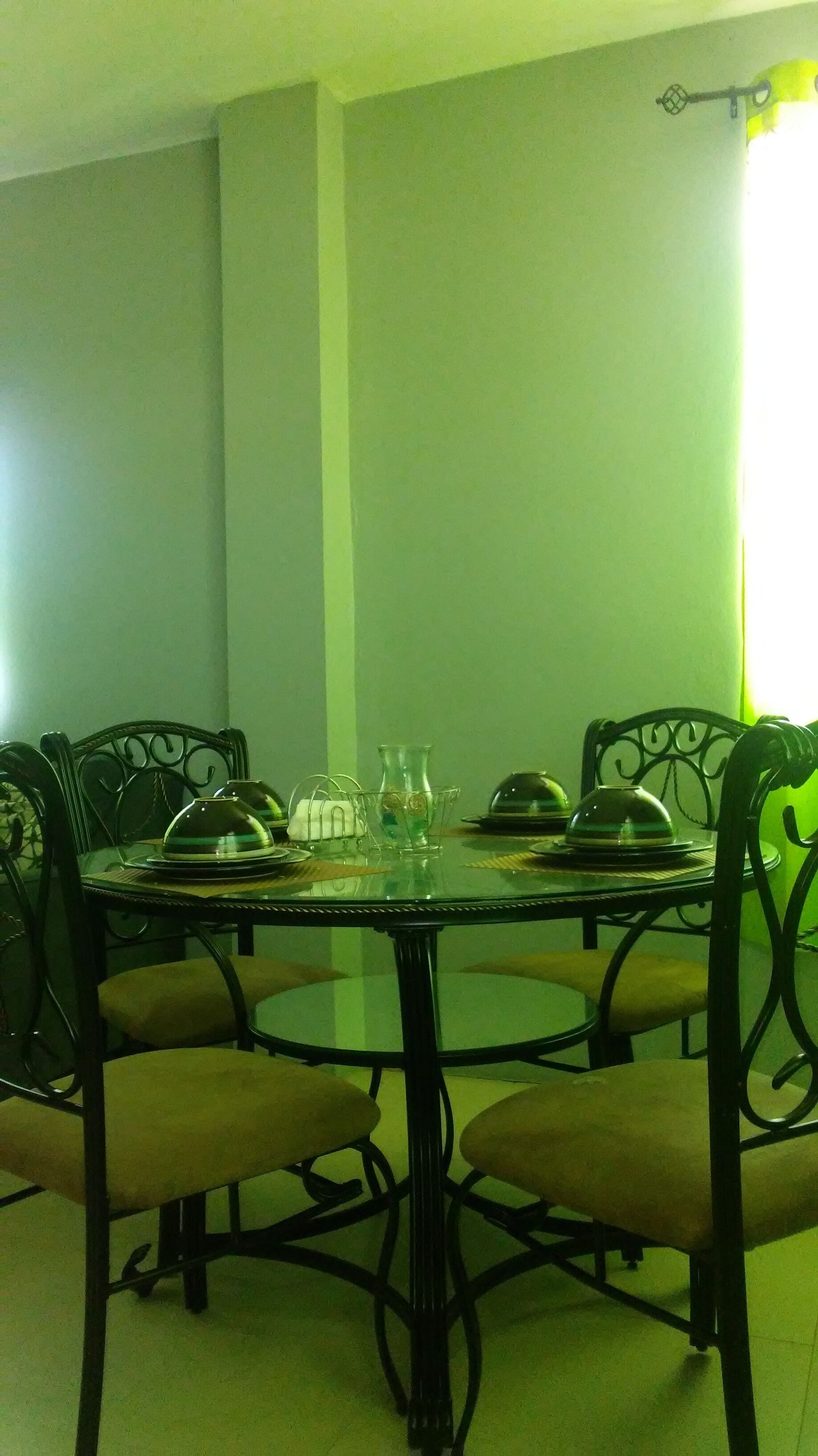 Un comedor con una mesa redonda de cristal, cuatro sillas y una araña.
