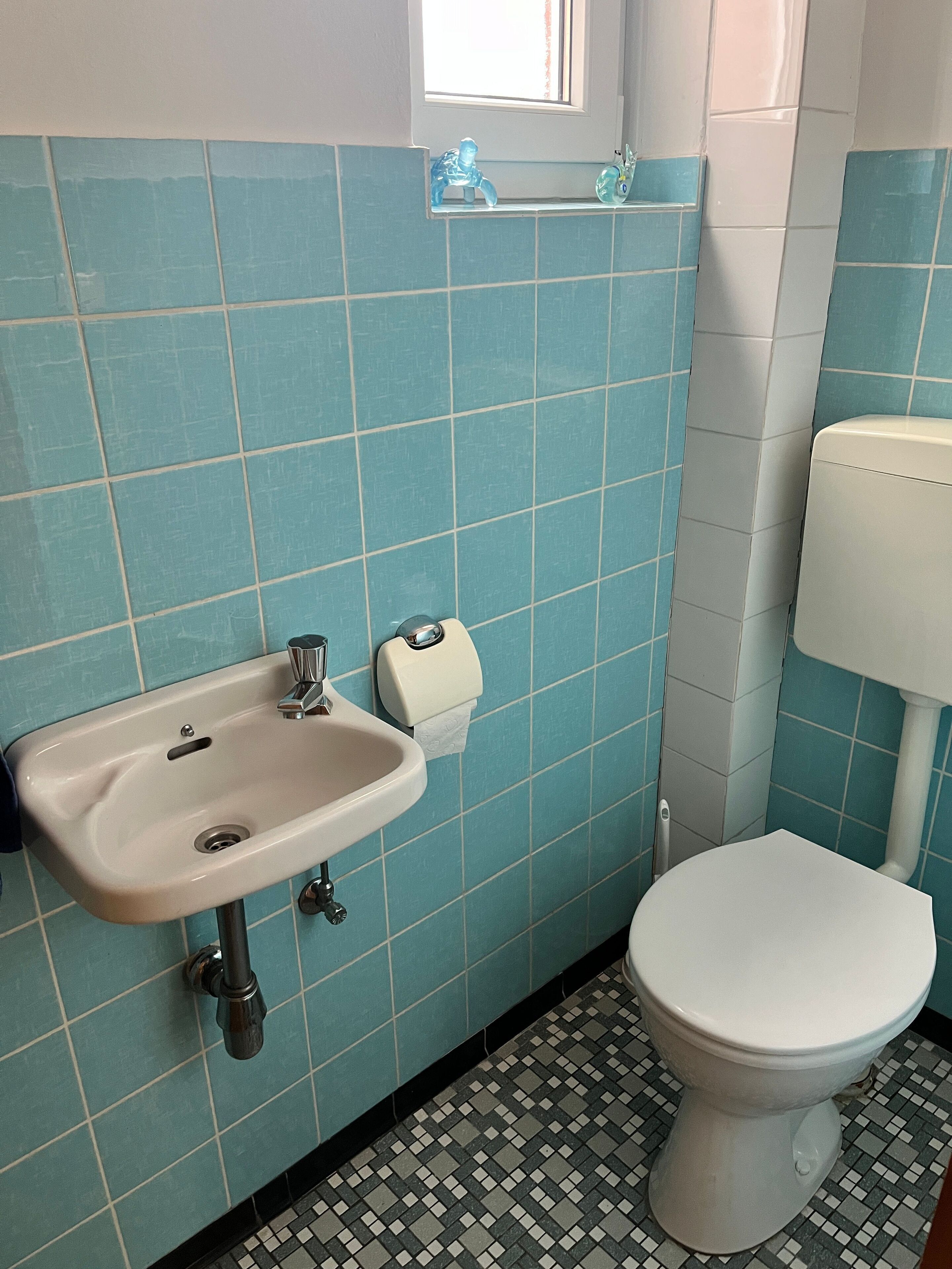 Un baño con lavamanos, inodoro y paredes cubiertas de azulejos azules.