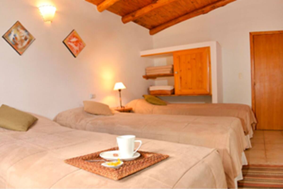 A hotel room with two beds, a wooden ceiling, a nightstand with a lamp, and a door.