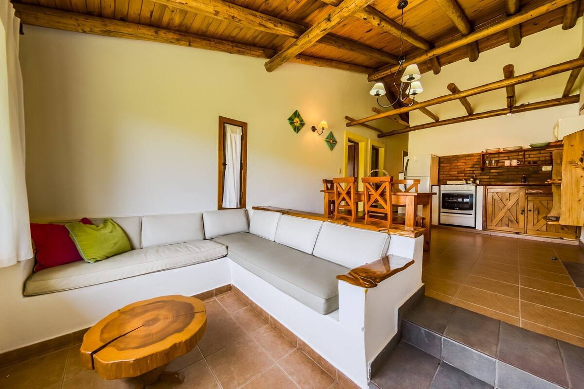 A living room with a sectional sofa, wooden coffee table, and a kitchen area with wooden cabinets and appliances.