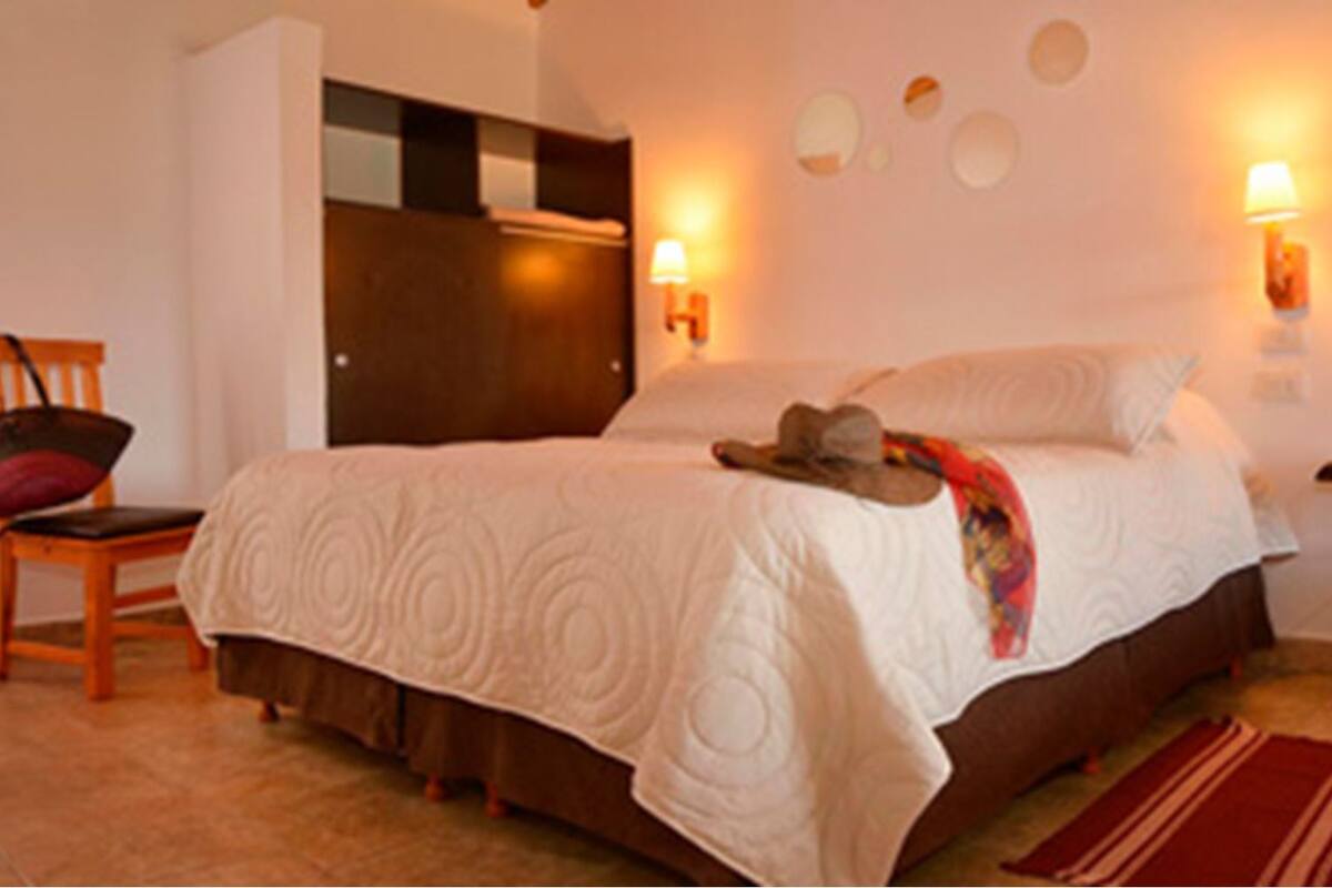 A bedroom with a bed, a chair, a nightstand, and wall sconces.