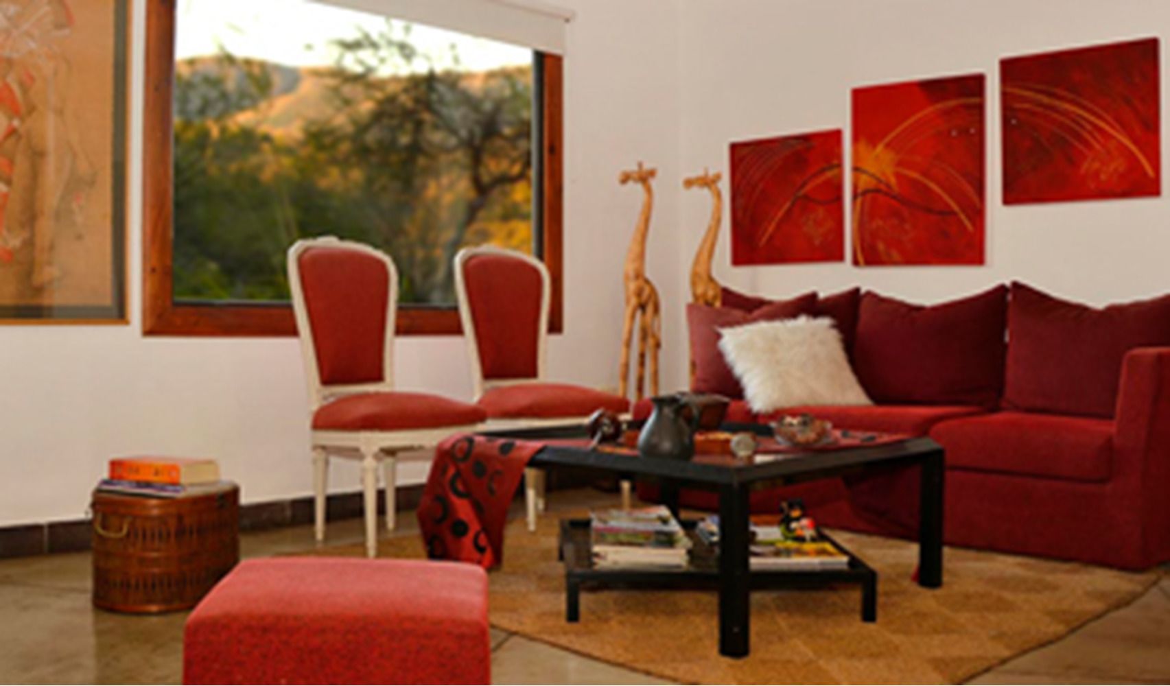 A living room with a red sofa, two red armchairs, a coffee table, and a giraffe statue. There are three red abstract paintings on the wall.