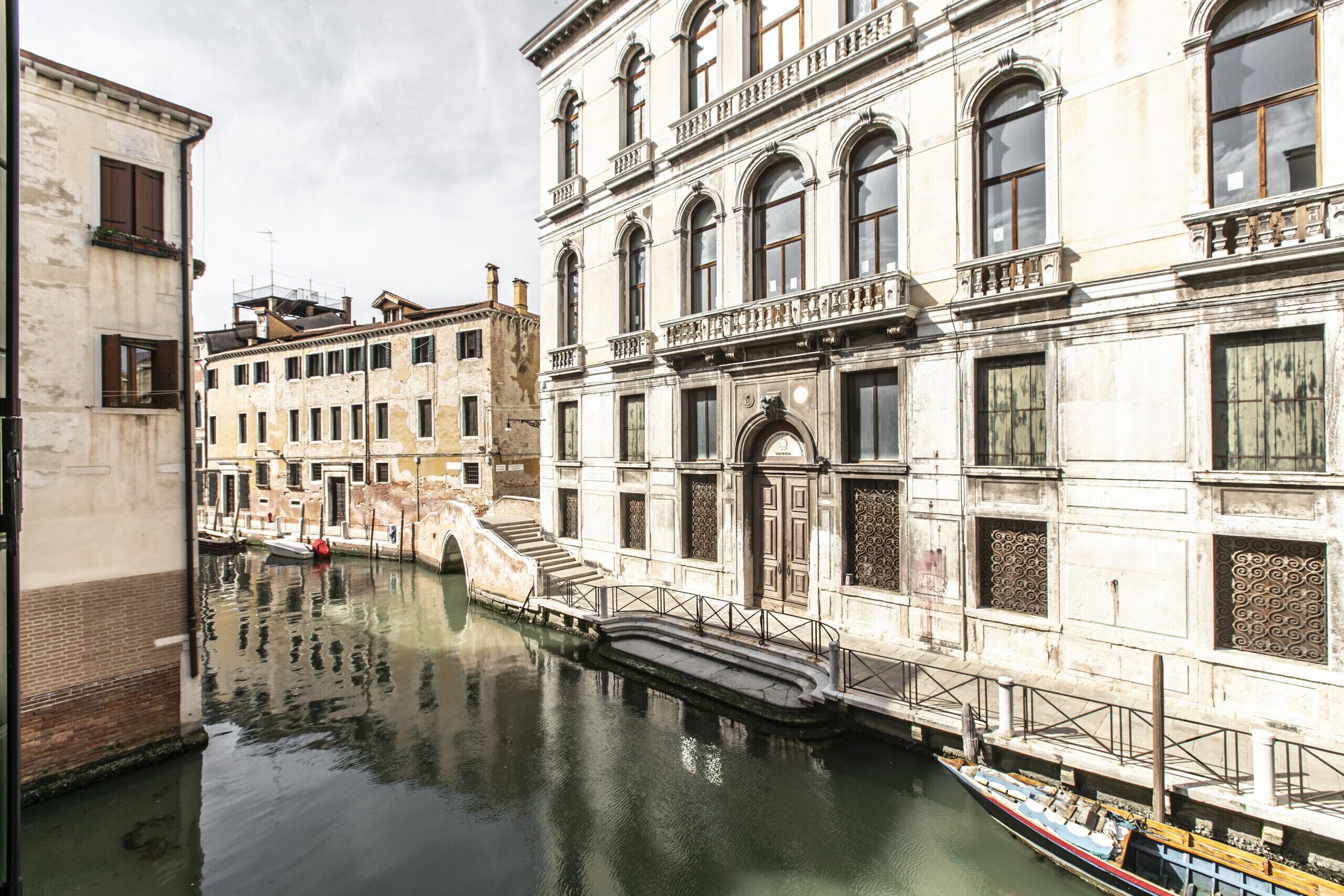 A canal with a boat docked at a building with ornate architecture and a staircase leading to a door.