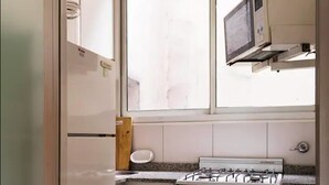 Une cuisine de taille réduite avec des meubles blancs, une cuisinière à gaz et un four à micro-ondes.
