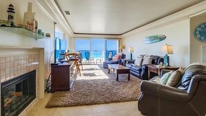 A spacious living room with a fireplace, a sofa, a coffee table, and a view of the ocean through large windows. - Ocean Front House with Private Ground Level Patio & 2 Garages - Sleeps 10+ (San Diego)
