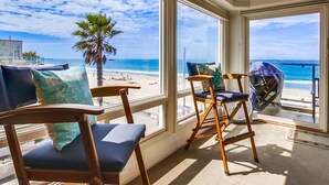 A room with large windows overlooking a beach, featuring wooden chairs and a view of the ocean. - Ocean Front House with Private Ground Level Patio & 2 Garages - Sleeps 10+ (San Diego)