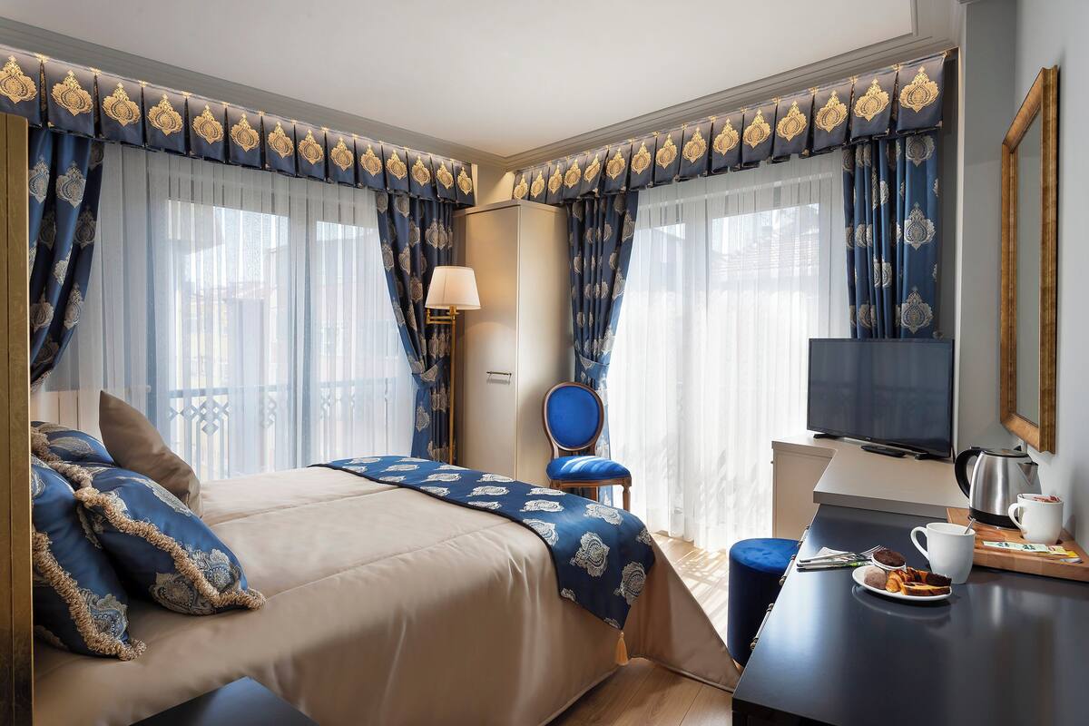 Hotellihuone, jossa on sänky, kirjoituspöytä, kahvikuppi, tuoli ja televisio.