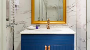 Ein Badezimmer mit einer Marmorwand, einem weißen Waschbecken, einer blauen Kommode und einem spiegel mit goldener Rahmung.
