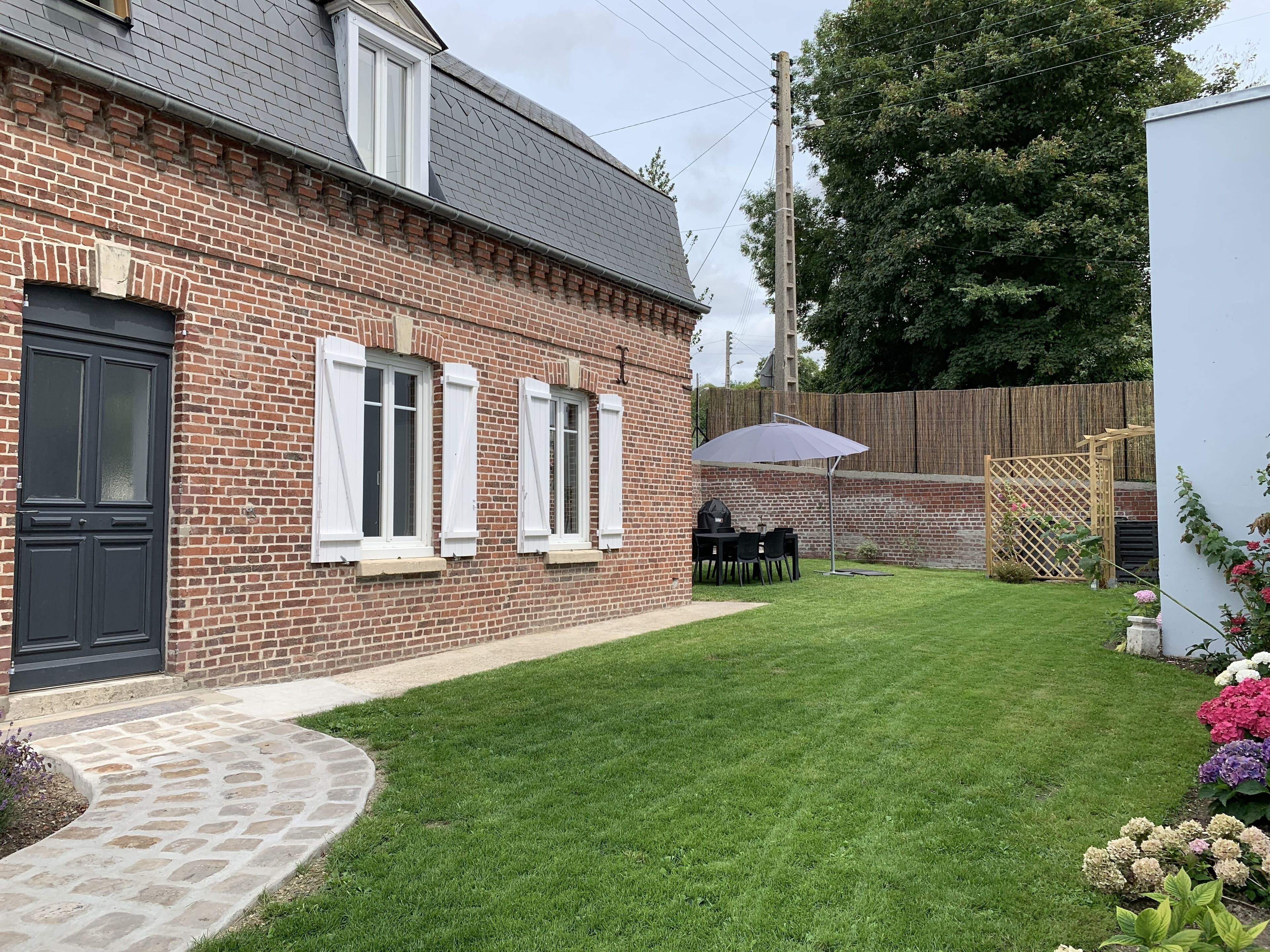 A brick house with a stone pathway, a lawn, and a wooden fence.