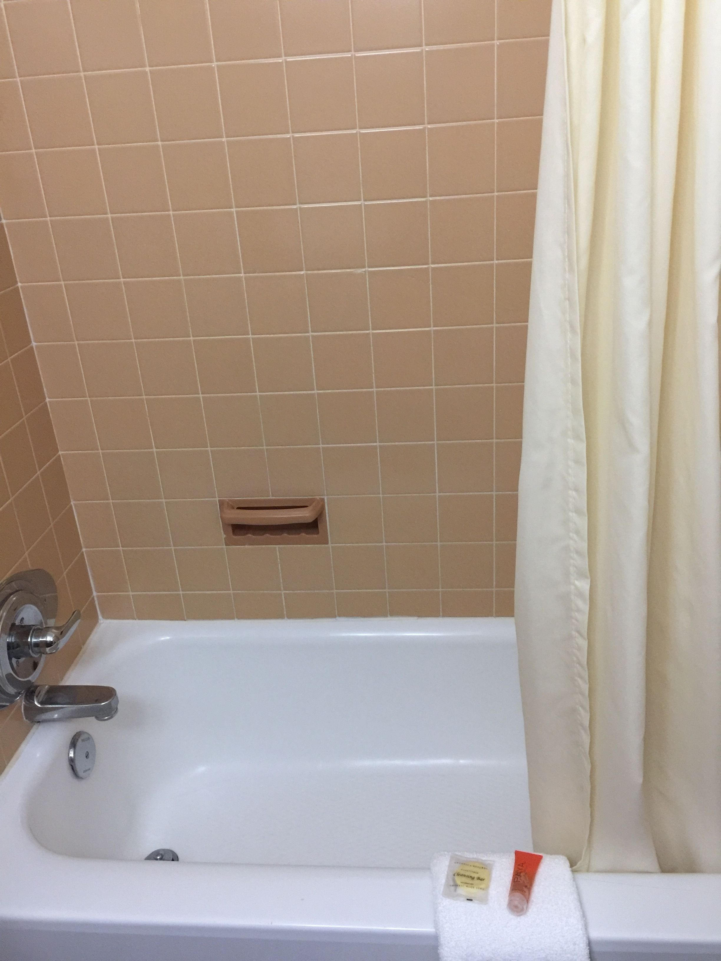 A bathroom with a bathtub, beige tiles, a towel, and a shower curtain.