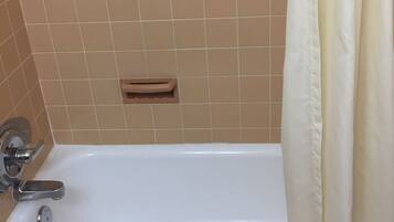 A bathroom with a bathtub, beige tiles, a towel, and a shower curtain.