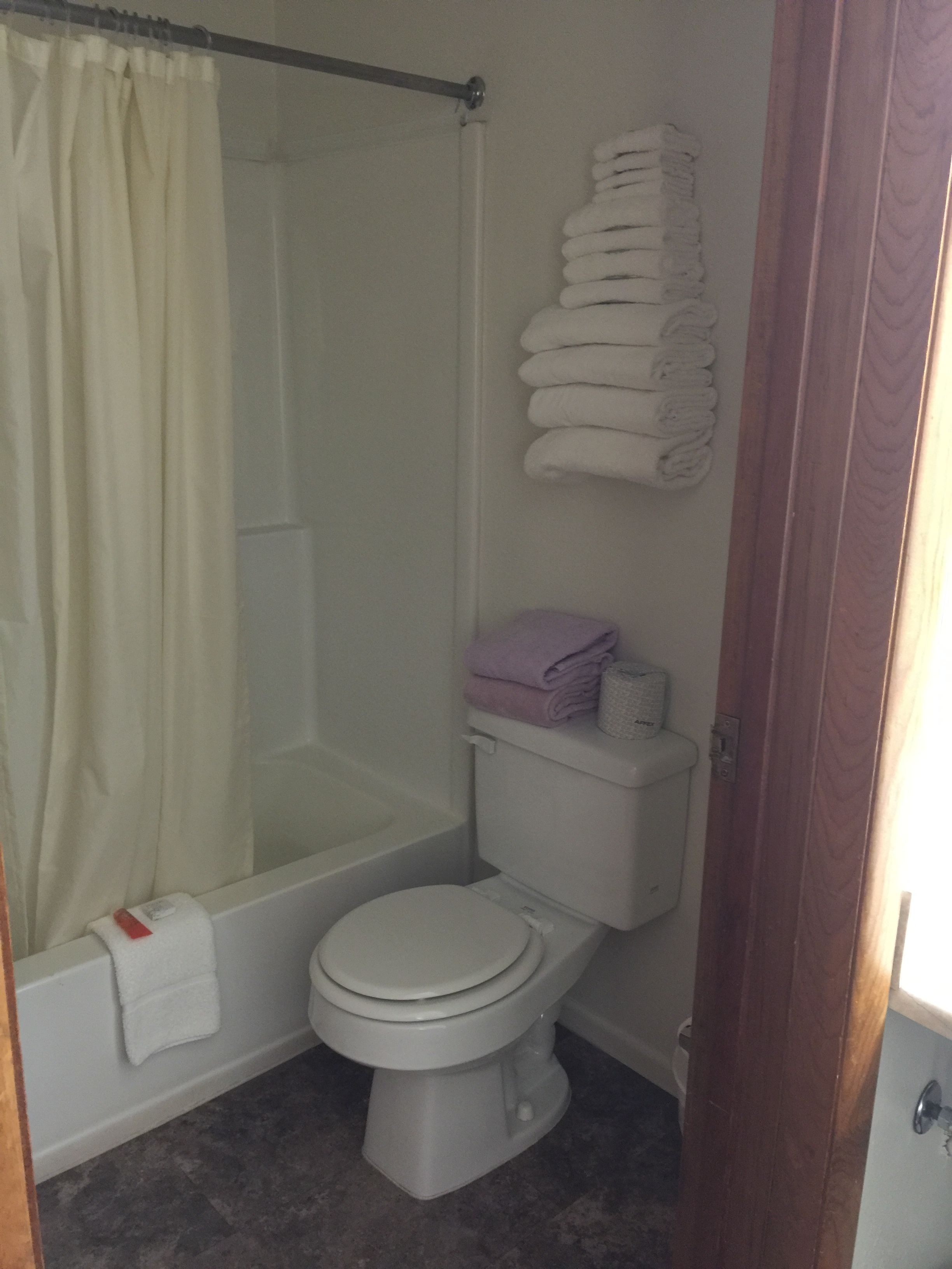 A bathroom with a shower, toilet, and a stack of towels on the wall.