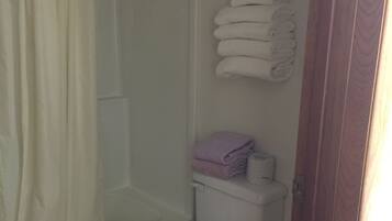 A bathroom with a shower, toilet, and a stack of towels on the wall.