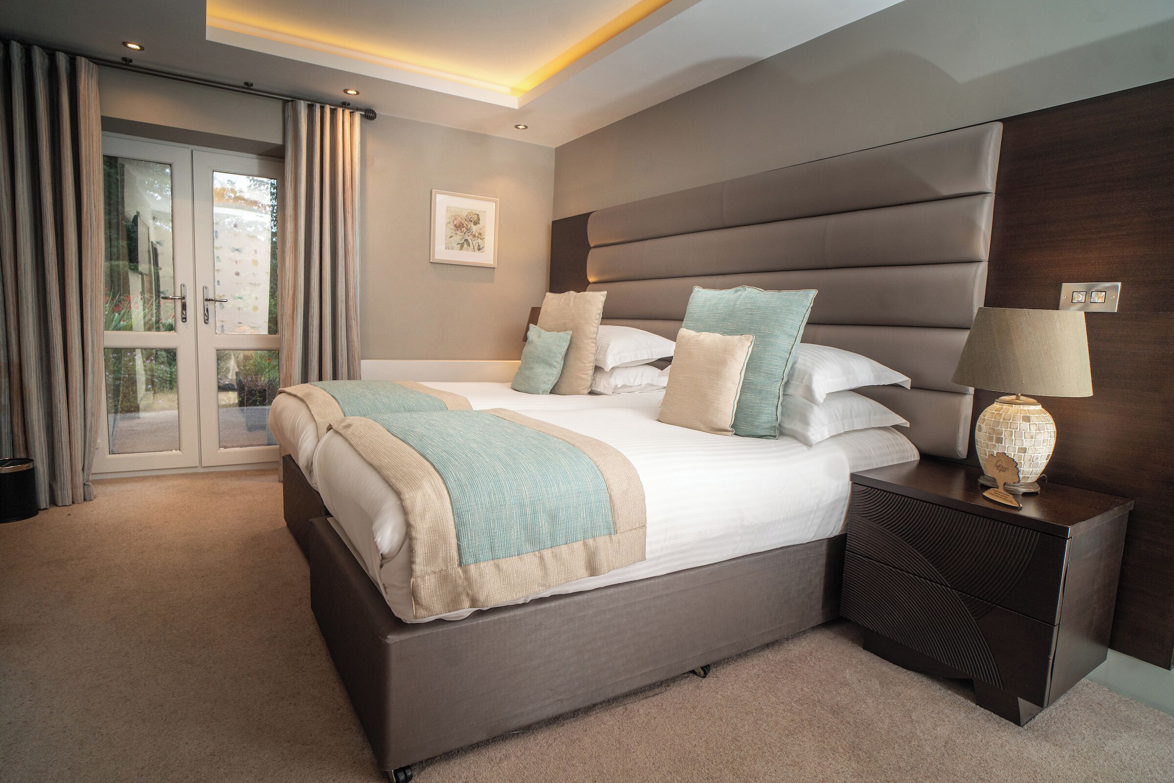 A bedroom with a large bed, a nightstand, a lamp, and a sliding glass door.
