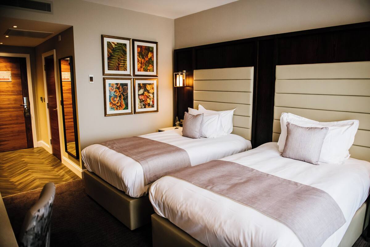 Habitación de hotel con dos camas, piso de madera y una pared decorada con cuadros.