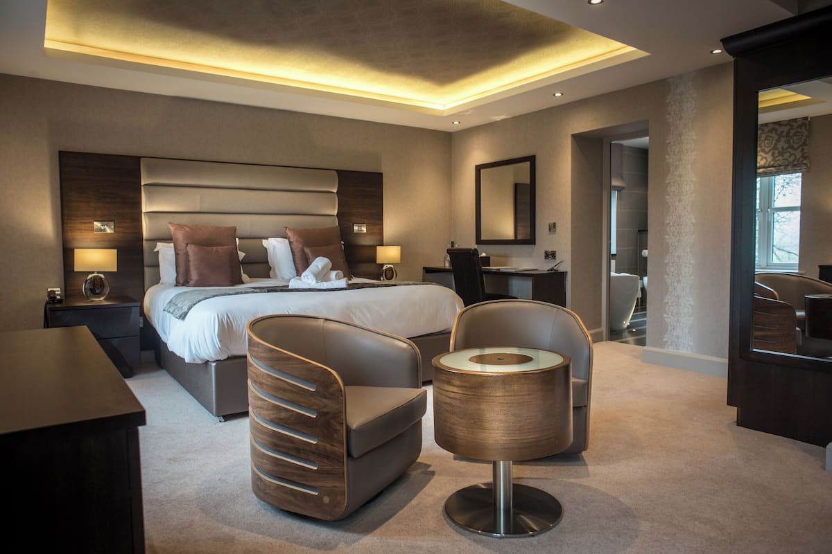 Una habitación de hotel moderna con una cama grande, una zona de estar con una silla y una mesita, y un escritorio separado.