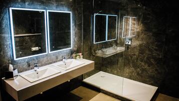 A modern bathroom with two sinks, a large mirror, and a separate shower area.