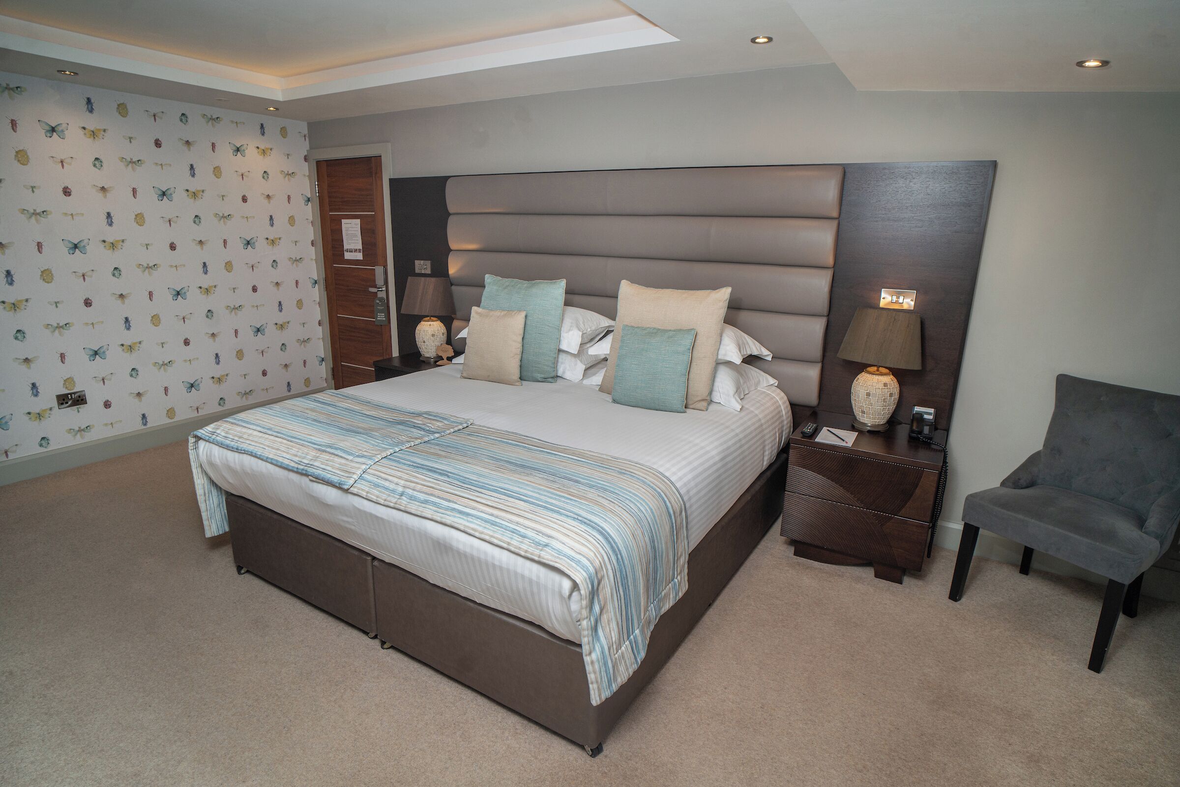 A modern bedroom with a large bed, two bedside tables, a chair, and a wall with butterfly decals.