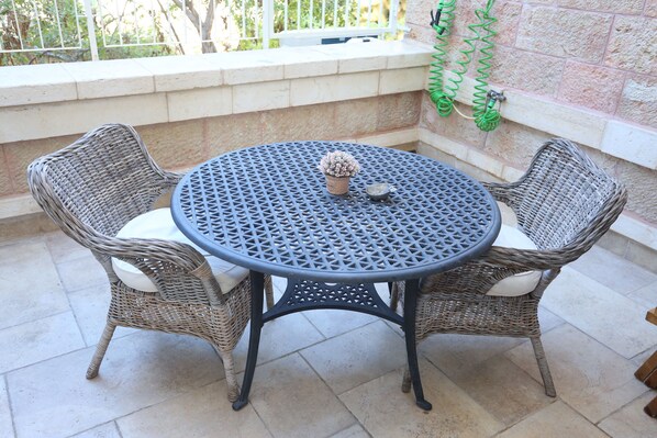 A round metal table with a woven wicker chair on each side. - Authentic luxurious modern fully equipped flat (Jerusalem)