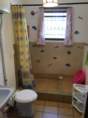 A bathroom with a toilet, shower curtain, tiled walls, and a window.