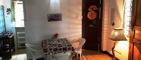 Un coin repas avec une table dressée pour quatre personnes, des chaises blanches, une nappe à motifs et une lampe fixée au mur.
