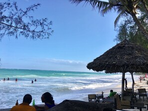 A beach scene with a thatched-roof hut, beach chairs, and people in the water.