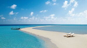 Una playa con aguas turquesas cristalinas, un bote y sillas de descanso.