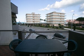 En balkon med et bord og stole, udsigt over en gade med biler og bygninger.