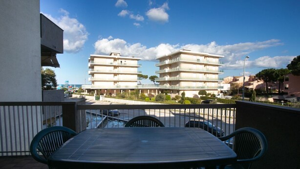 Ein Balkon mit Tisch und Stühlen, der auf ein Gebäude mit mehreren Balkonen und einem klaren Himmel blickt.