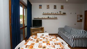Ein Wohnzimmer mit Fernseher, einem gestreiften Sofa, einem Esstisch mit Speisekarte und einem Deckenventilator.