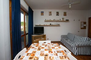 Un salon avec un téléviseur, un canapé à rayures, une table à manger avec un menu, et un ventilateur de plafond.