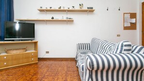 Ein Wohnzimmer mit Fernseher, Sofa, Holzregalen und Kunstwerken an der Wand.