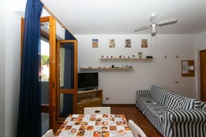A room with a TV, a striped sofa, a dining table with a menu, a ceiling fan, and shelves with decorative items. - M089 - Marcelli, three-room apartment with terrace 30 meters from the sea (Marcelli)