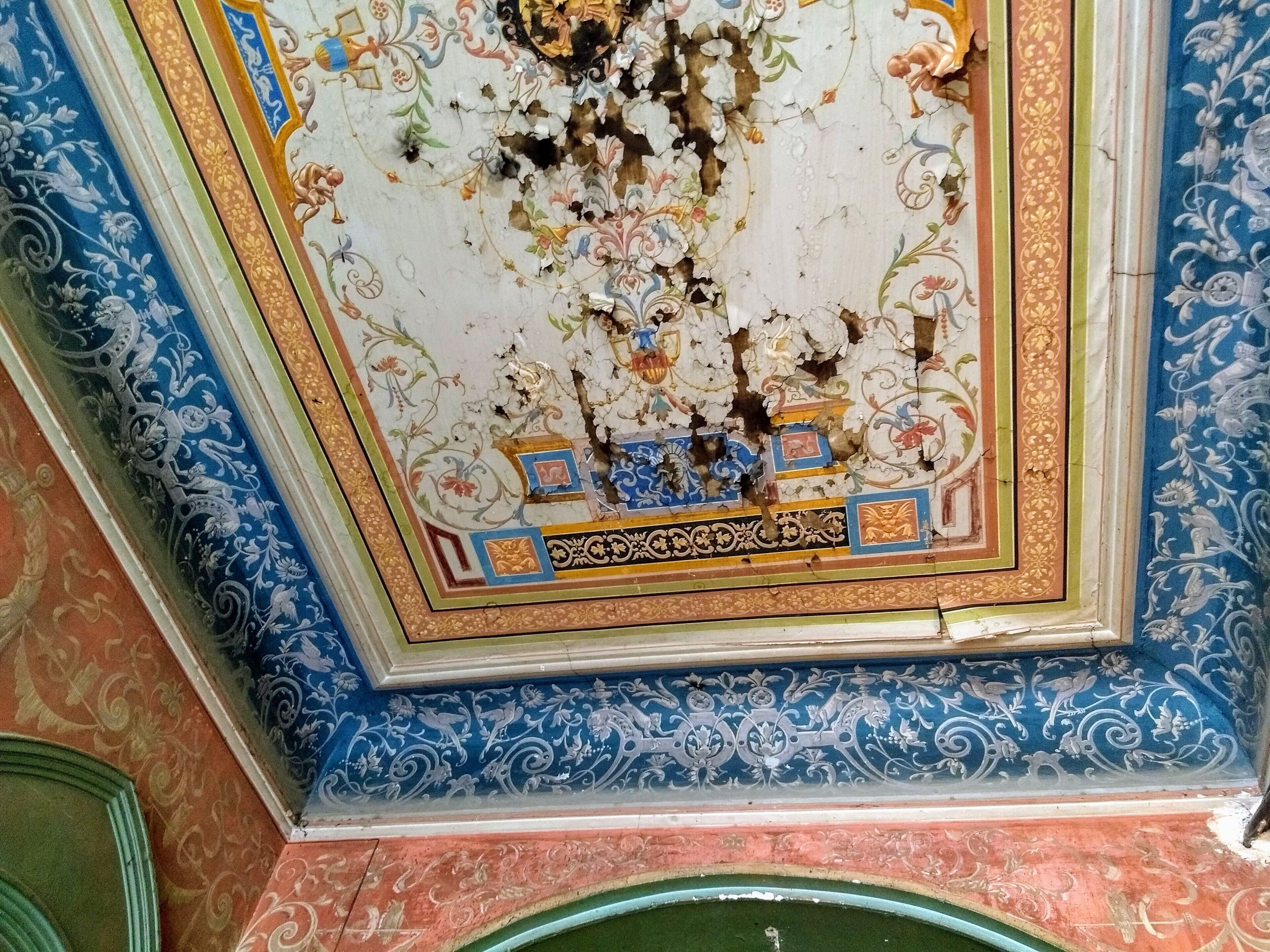 Een plafond met ingewikkelde bloemenmotieven en een beschadigd deel.