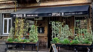 Ein Café mit schwarzem Markisenbalkon, Terrassensitzgelegenheiten und hängenden Pflanzen.