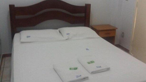 A bed with a wooden headboard, a small bedside table, and a framed picture on the wall. - Ami Hotel (Varzea Grande)