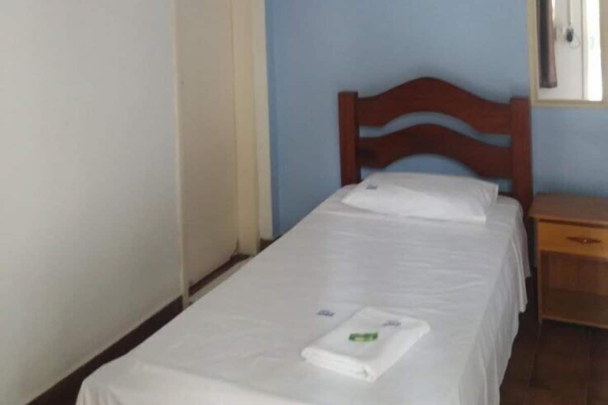Una cama individual en una habitación con cabecera de madera, una mesita de noche pequeña y un equipo de aire acondicionado instalado en la pared.